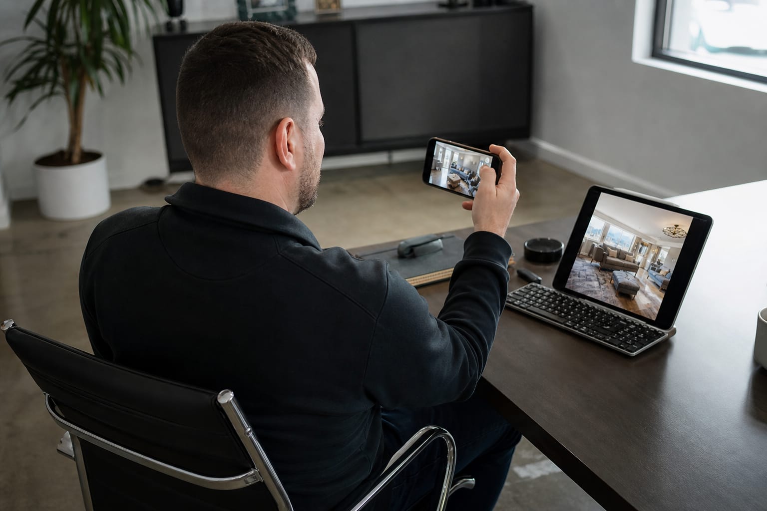 Sales rep holding a smartphone as a customer's living room shows on a tablet for a video estimate walkthrough.