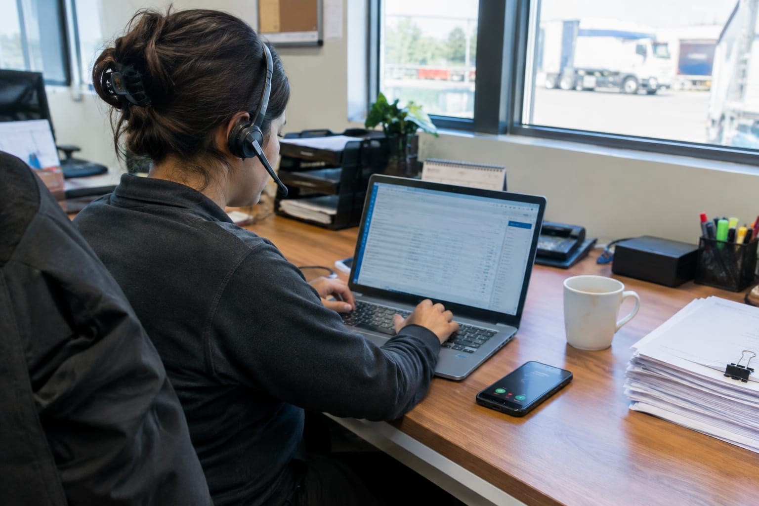 Coordinator on a headset typing a lead into a laptop while a second phone rings unanswered