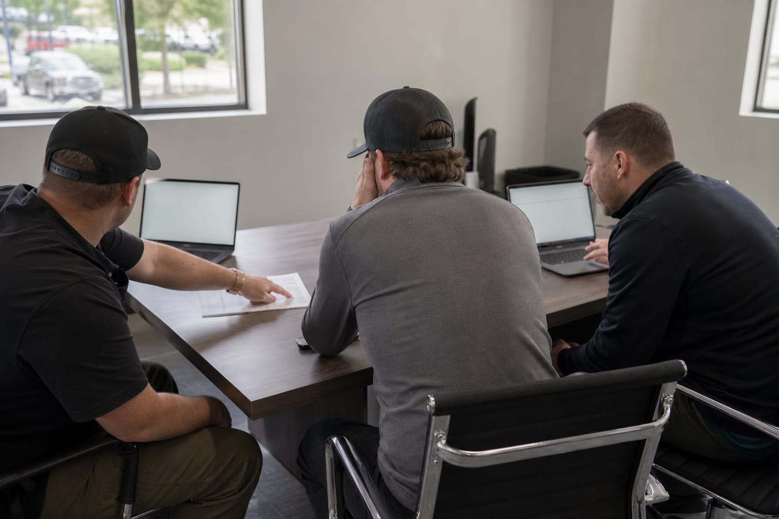 Three moving company managers reviewing a printed software vendor shortlist at a conference table.