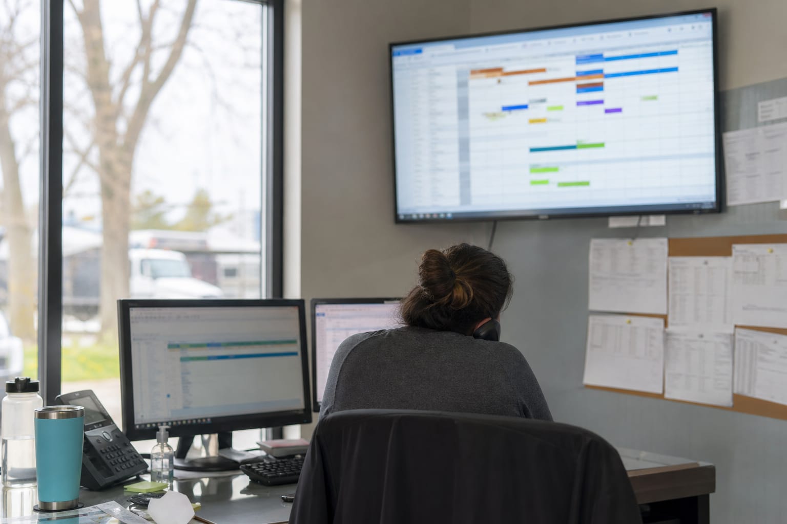 Dispatcher watching a wall screen of crew job statuses while on the phone in a moving office.