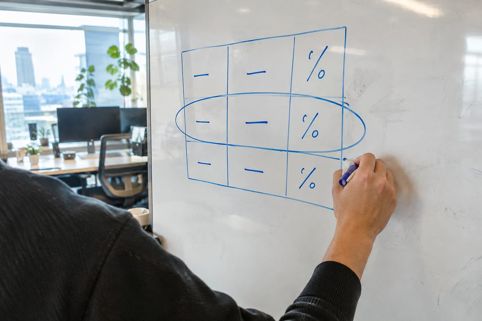Hand circling one row of a three-tier commission table drawn in marker on a smudged office whiteboard.