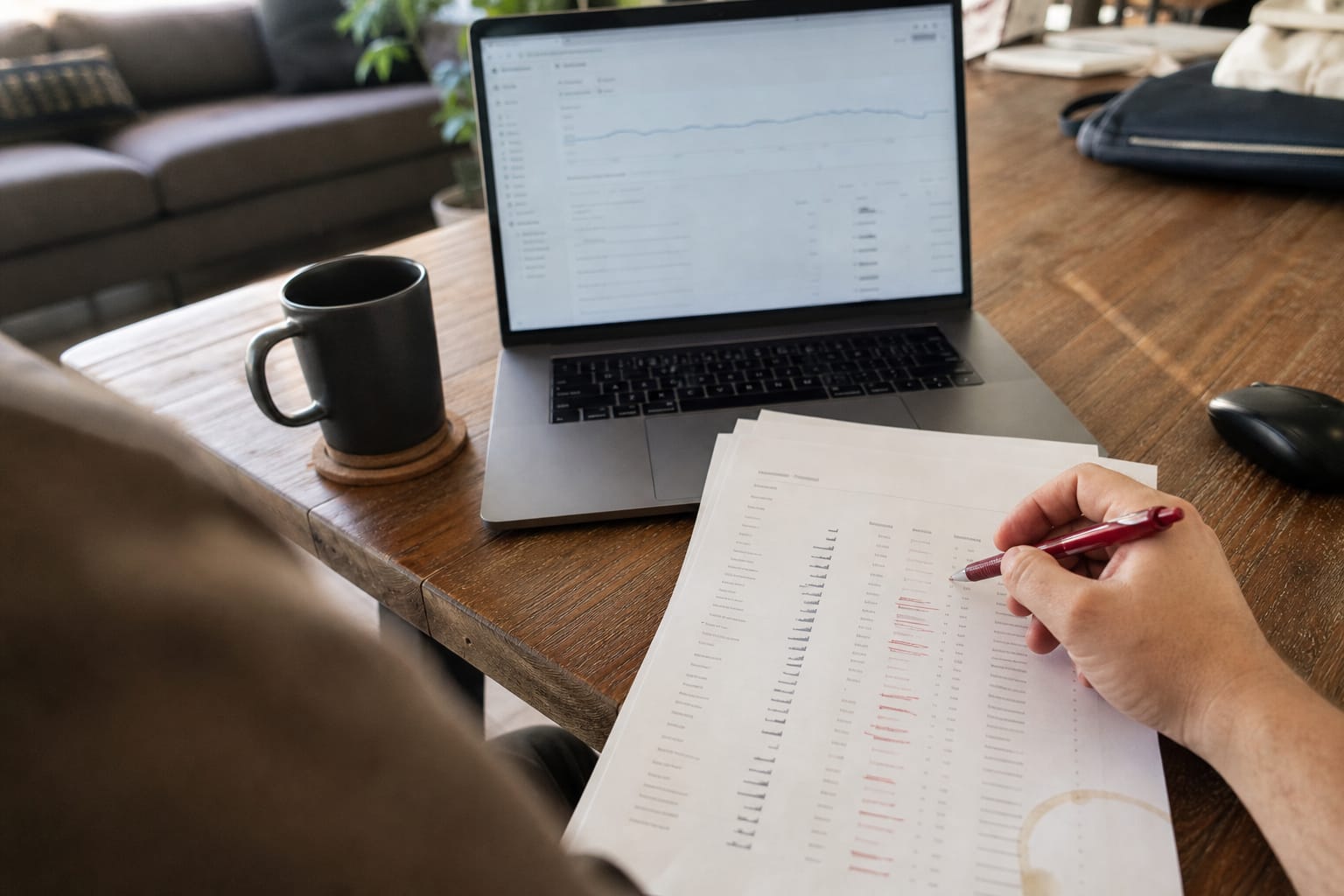 Hand crossing out irrelevant search queries on a printed search terms report with a red pen