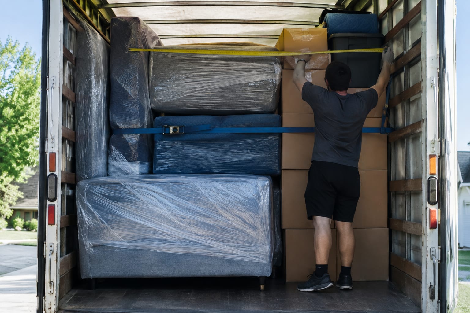 Inside a partially loaded moving truck with padded furniture and boxes stacked floor to ceiling against the front wall